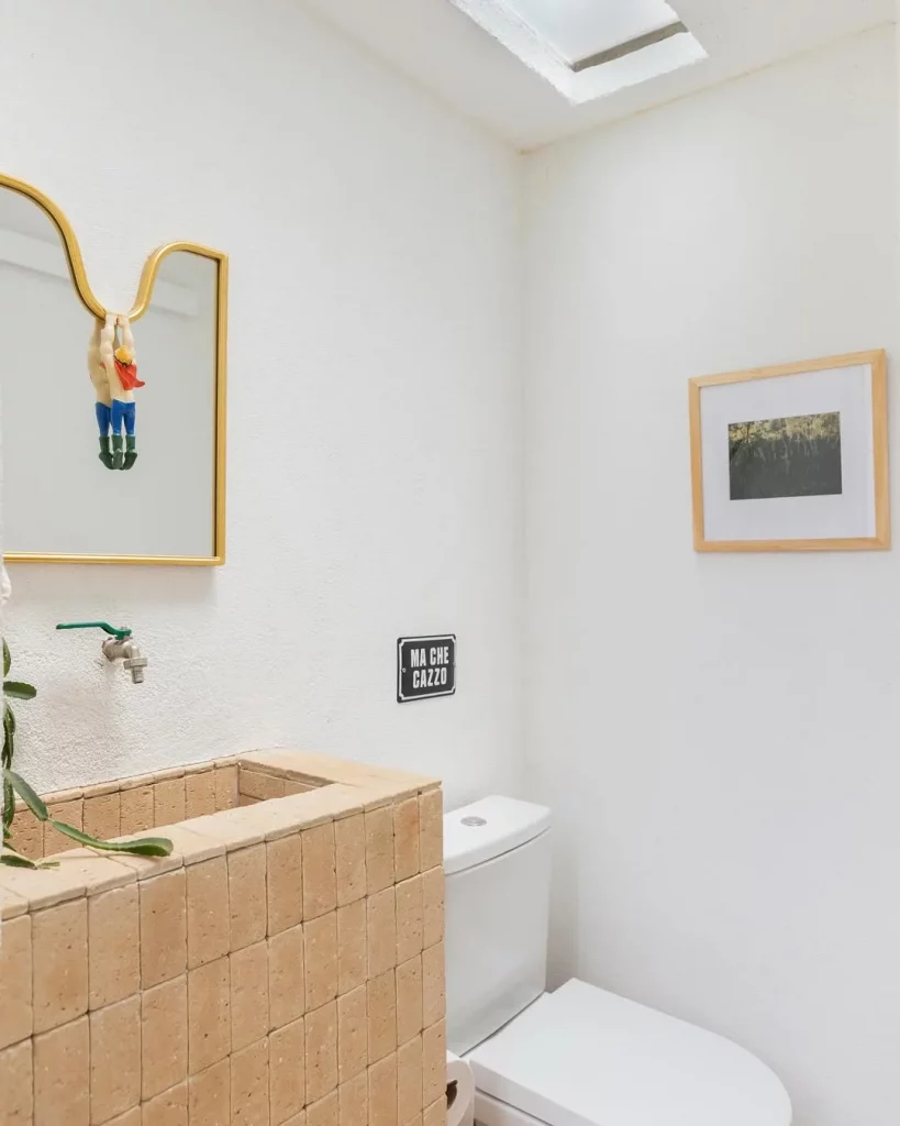 Banheiro pequeno com espelho diferente e boneco pendurado.