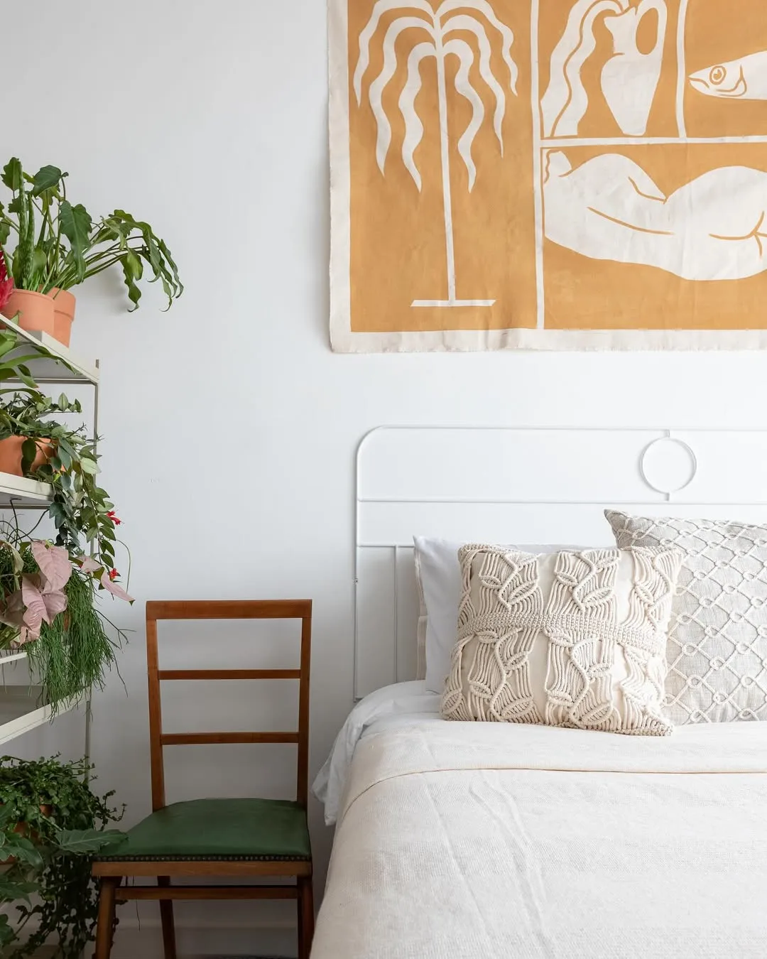 Cabeceira de metal pintada de branco como um relevo da parede e quadro de tecido acima da cama.
