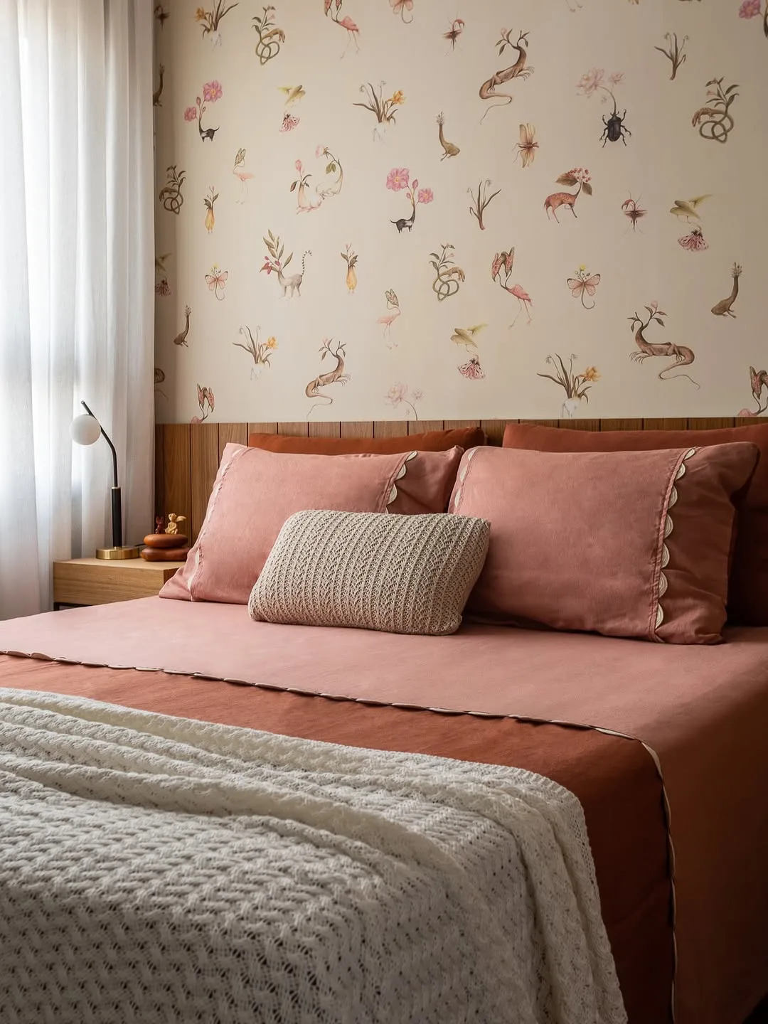 Cabeceira de cama discreta feita de madeira, com papel de parede e roupa de cama rosa.