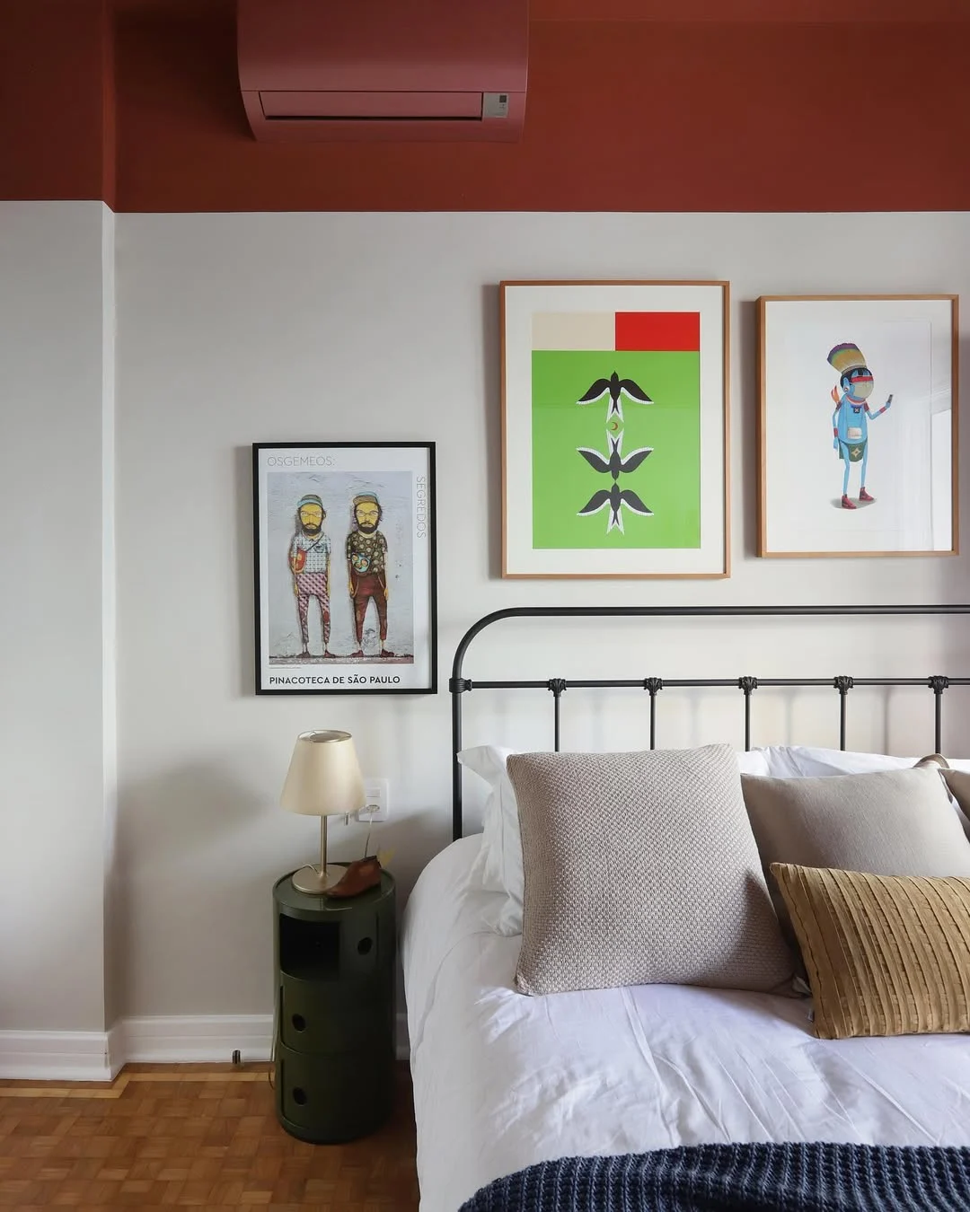 Cabeceira de cama de metal com extremidades arredondadas e quadros acima da cama, teto pintado de bordô.