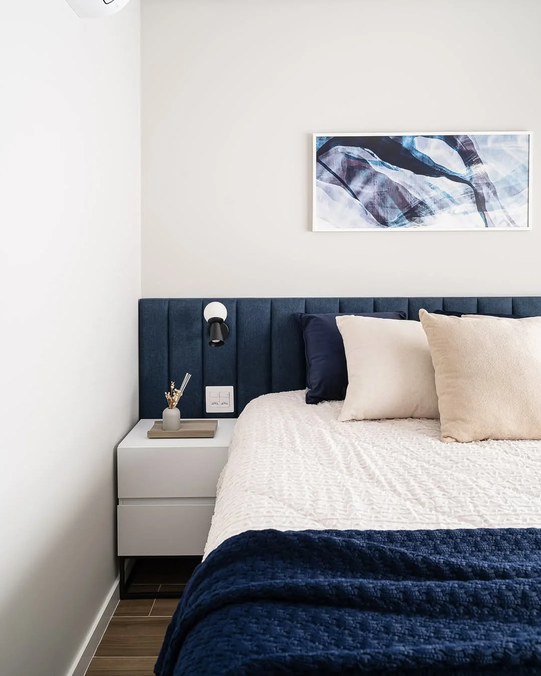 Cabeceira modular em tom de azul marinho combinando com a manta na cama.