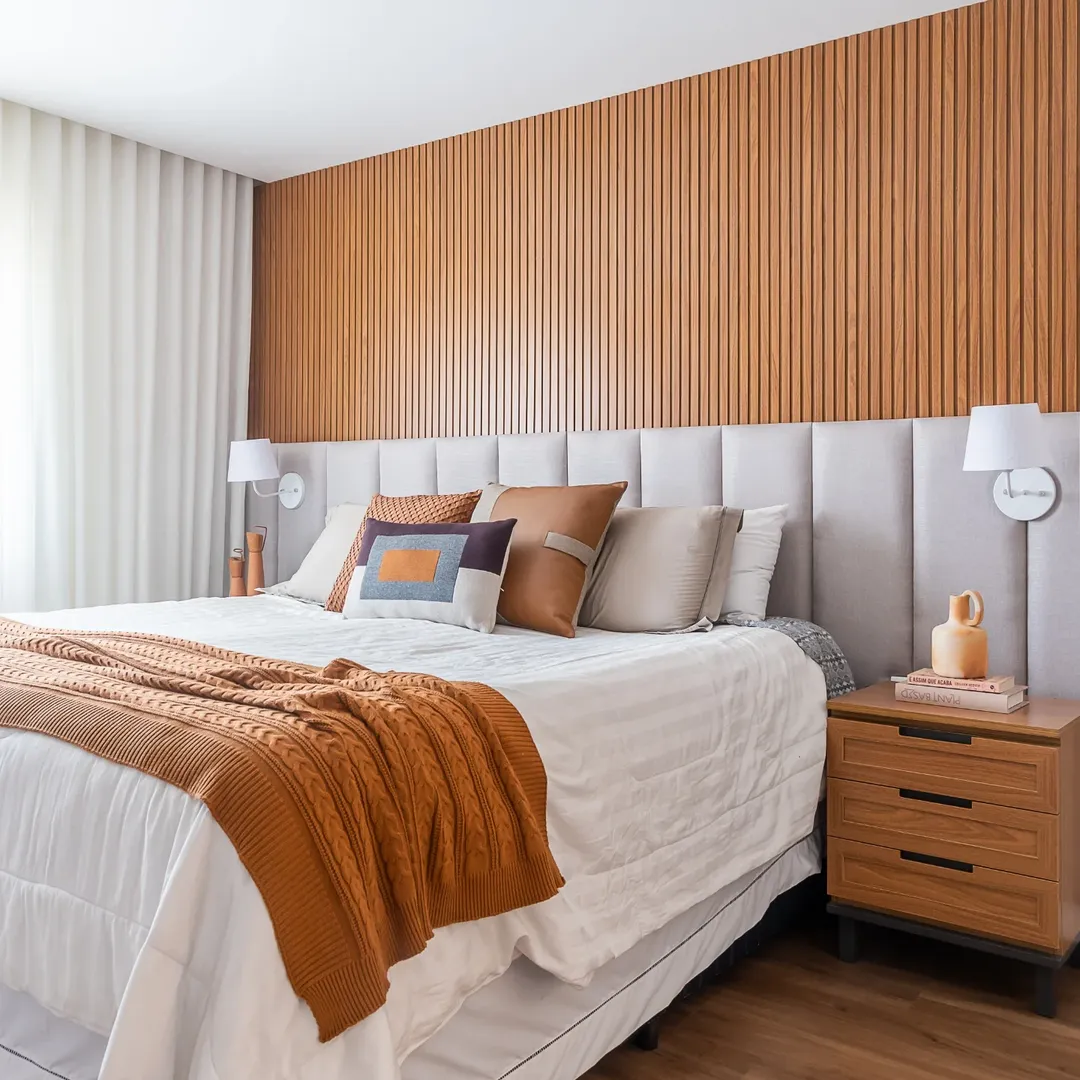 Painel ripado na parede com cabeceira modular cinza e manta na cama laranja.