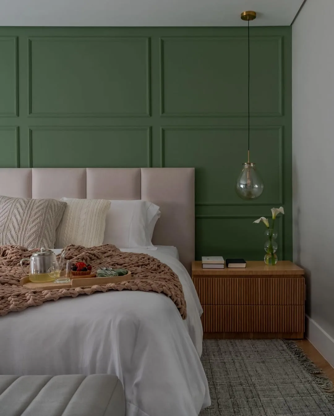 Cabeceira modular nude com parede verde e boiserie dando contraste.