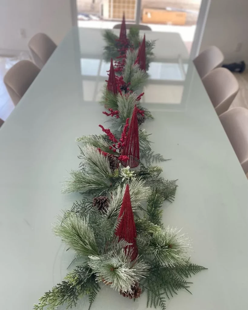 Centro de mesa de natal com cones vermelhos e folhagem na mesa.