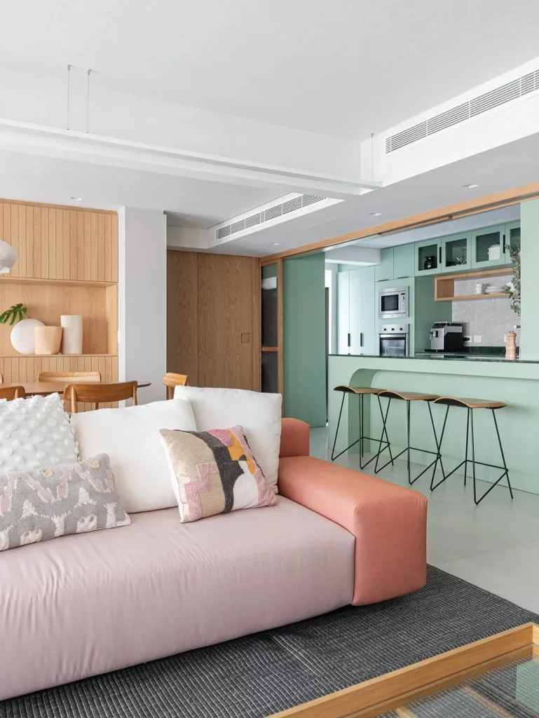 Sala e cozinha conjugada com bancada verde pastel e sofá rosa.