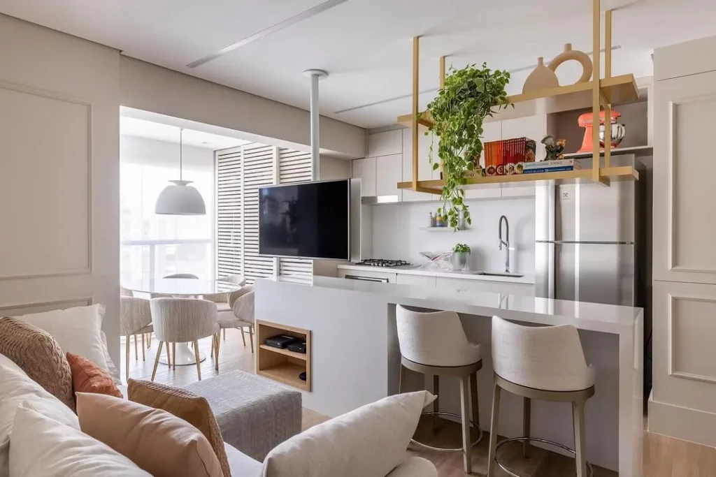 Cozinha e sala conjugada com televisão e móveis neutros.