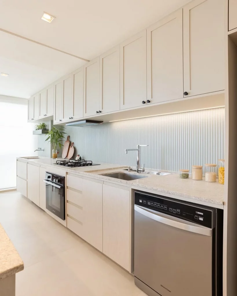 Cozinha linear em projeto minimalista, com tons claros e iluminação de LED nos armários.