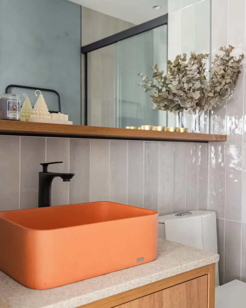 Cuba do banheiro laranja e prateleira abaixo do espelho.