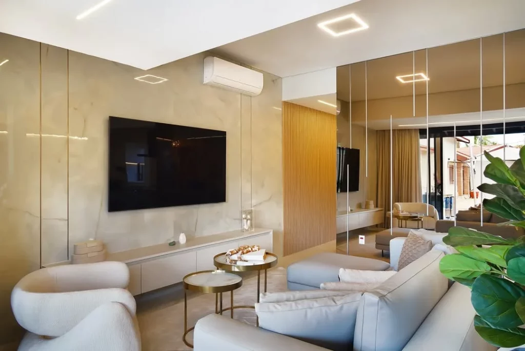 Painel de espelho com alguns LEDs espalhados, sala de televisão com sofá cinza e mesas de centro.