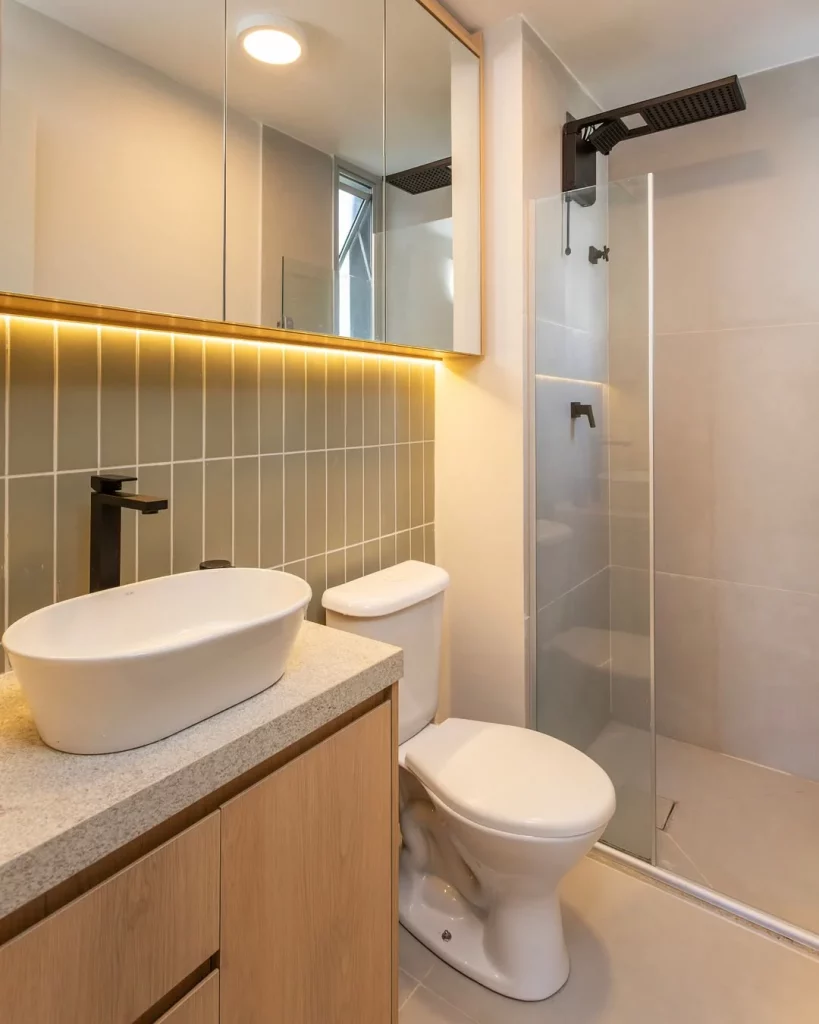 Espelho iluminado no banheiro pequeno com revestimento verde na parede.