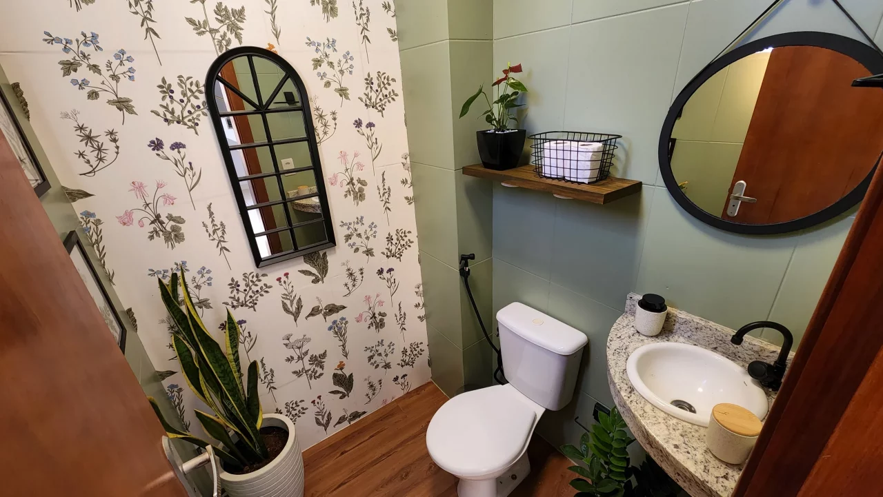 Lavabo redecorado com papel de parede floral, planta, espelho em formato de janela de vidro e prateleira.