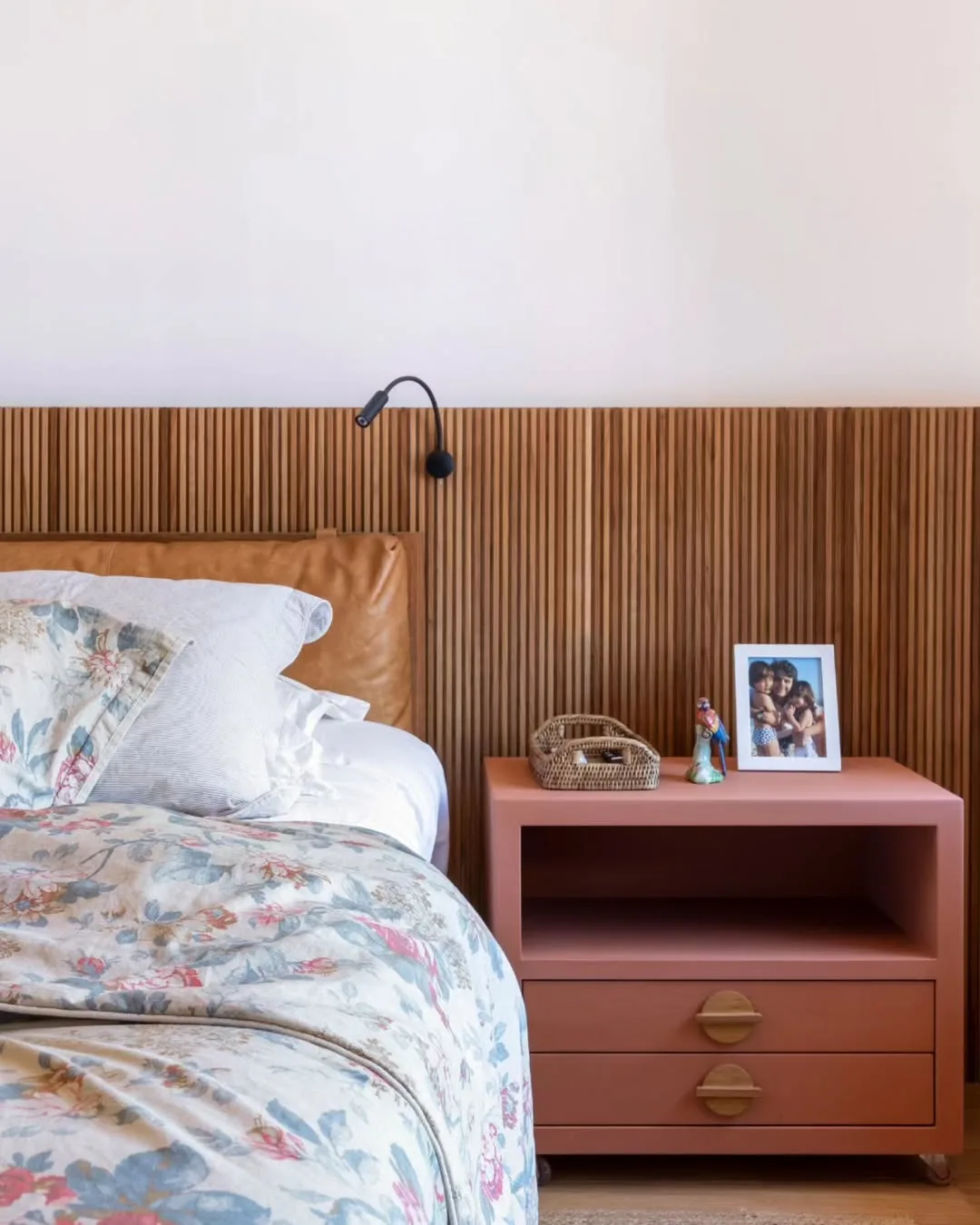 Cabeceira de cama com painel ripado de madeira e mesa lateral rosa.
