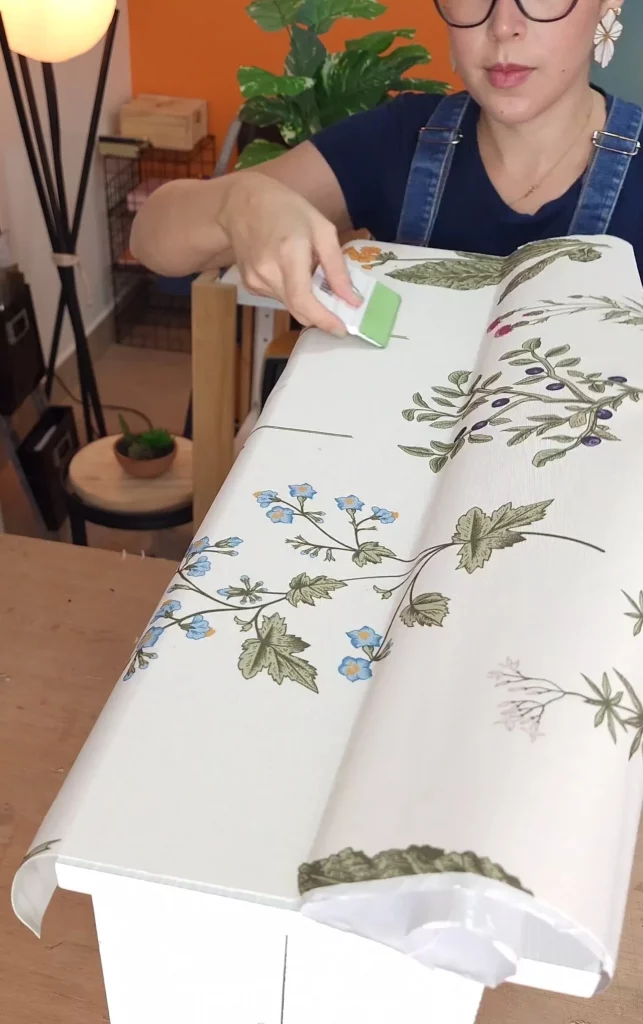 Instalando papel de parede floral na gaveta com ajuda de um cartão para espatular.
