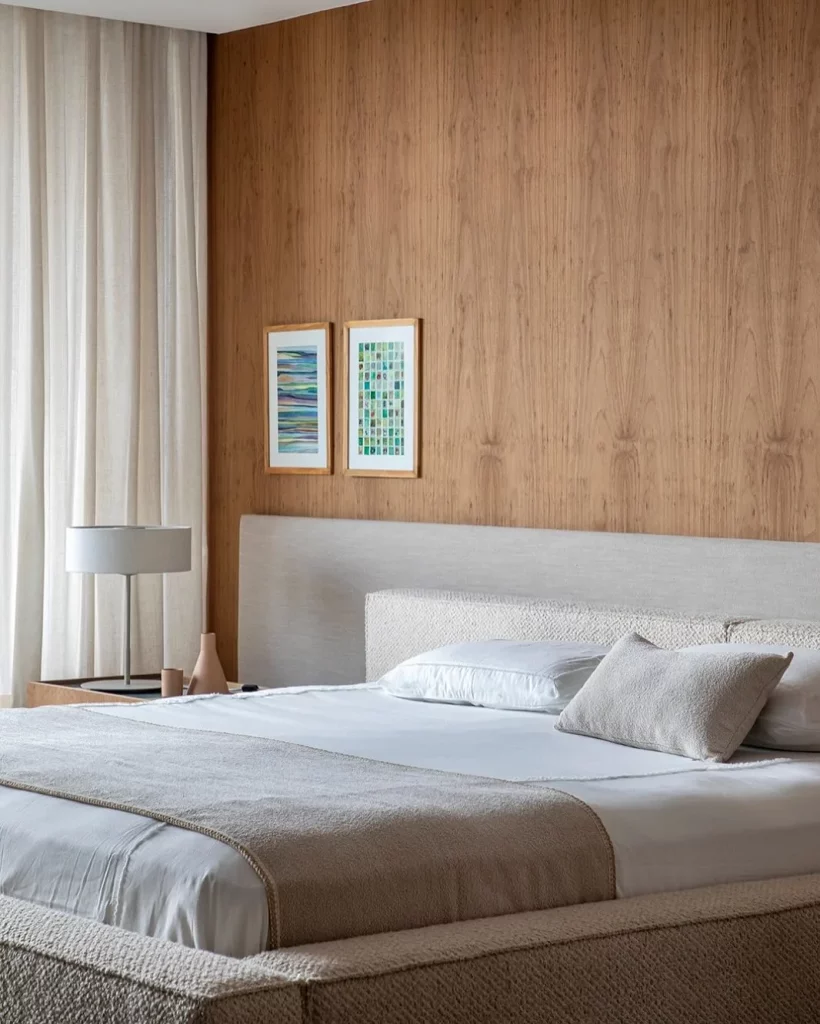 Parede de madeira no quarto minimalista com cabeceira cinza e quadros.