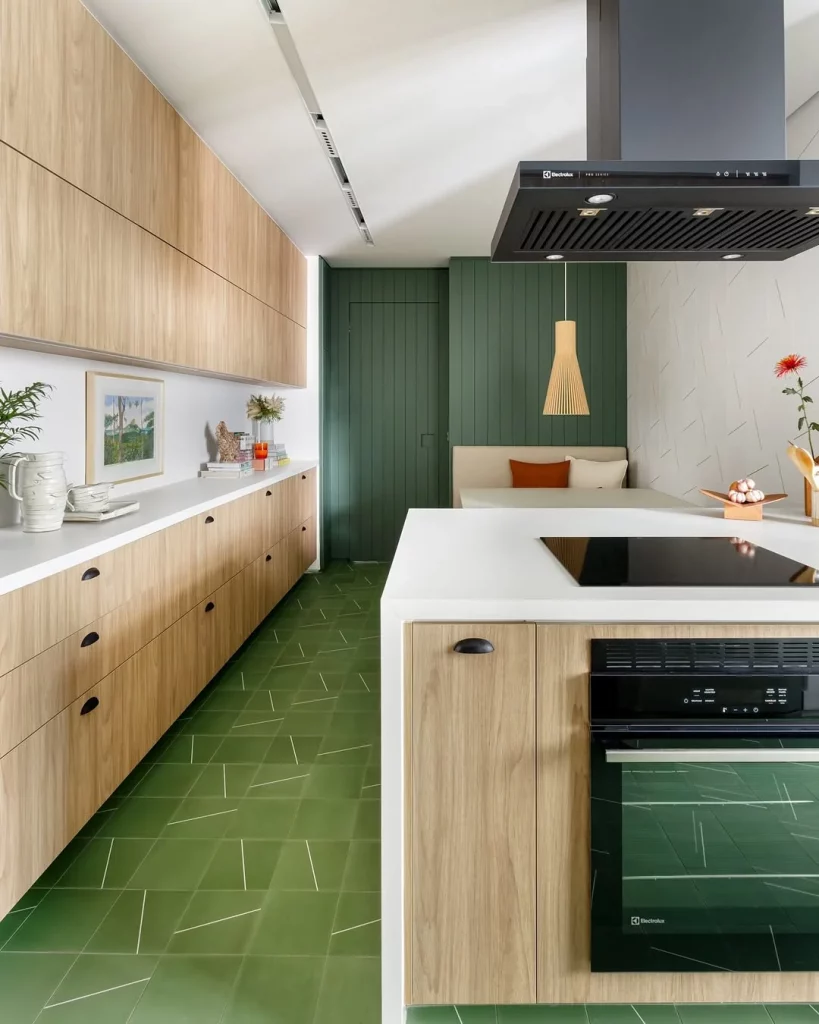 Cozinha com piso verde e armários de madeira, espaço compartilhado com mesa de jantar.