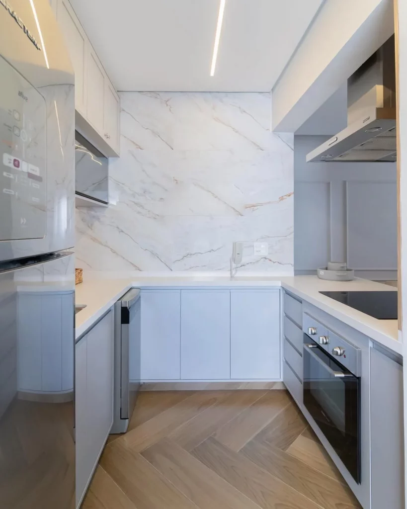 Piso porcelanato acetinado que imita madeira na cozinha de armários azuis e parede marmorizada.