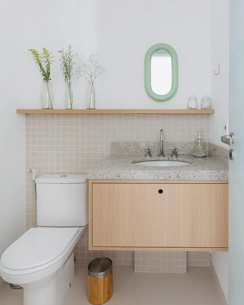 Prateleira madeira clara com vasos e espelho pequeno no lavabo.