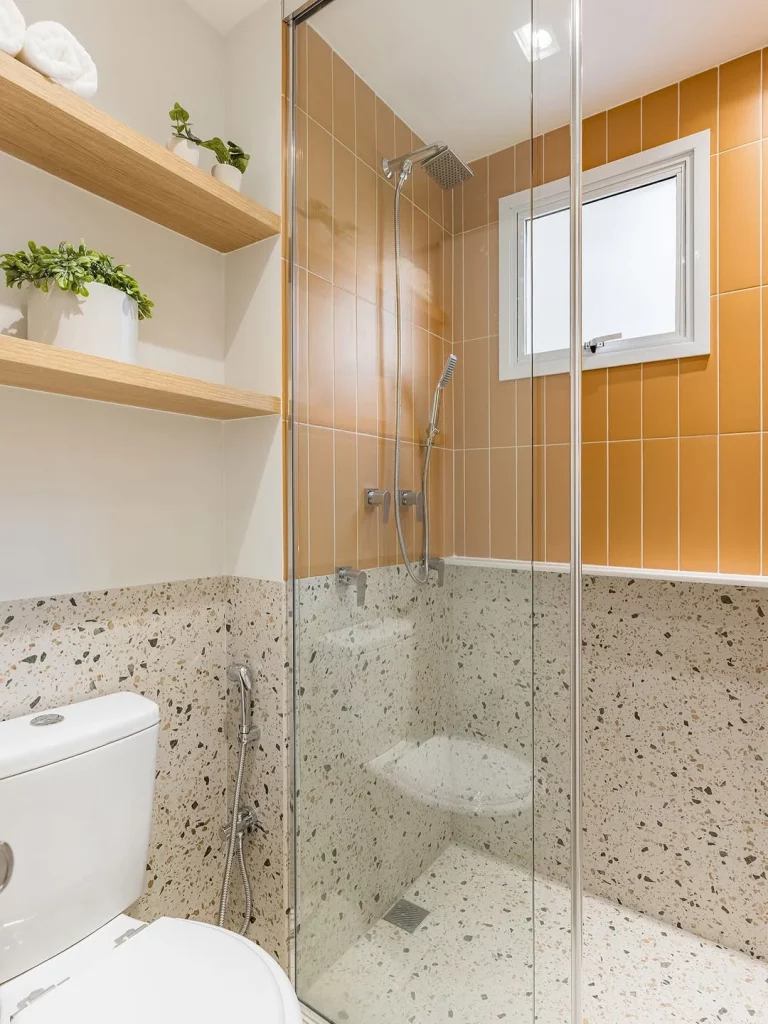 Prateleira de madeira acima do vaso e com azulejos laranjados no banheiro.