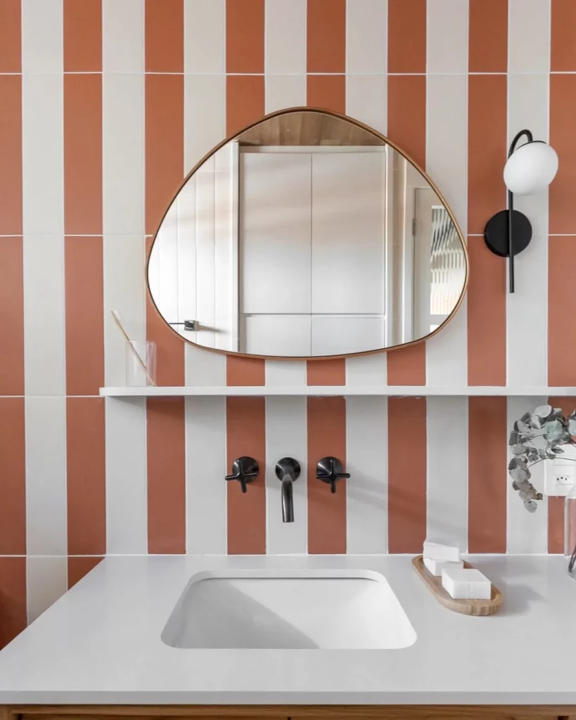 Prateleira branca abaixo do espelho na parede listrada.