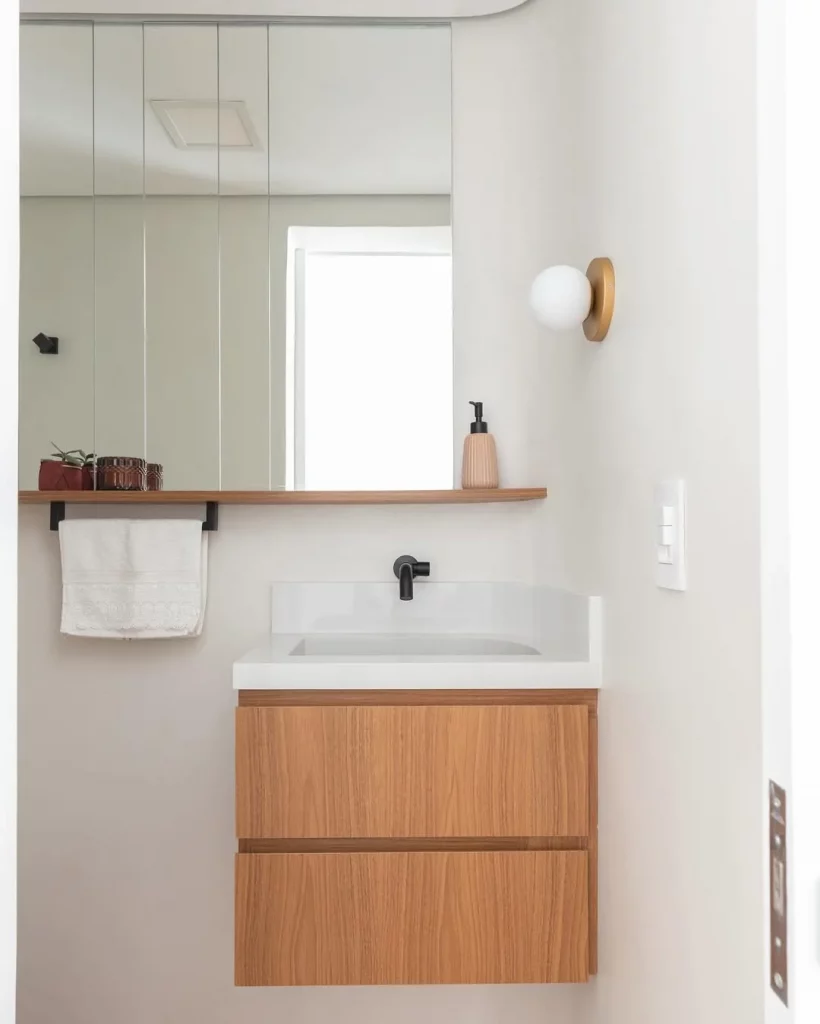 Banheiro peqeuno com prateleira perto do espelho e armário de madeira.