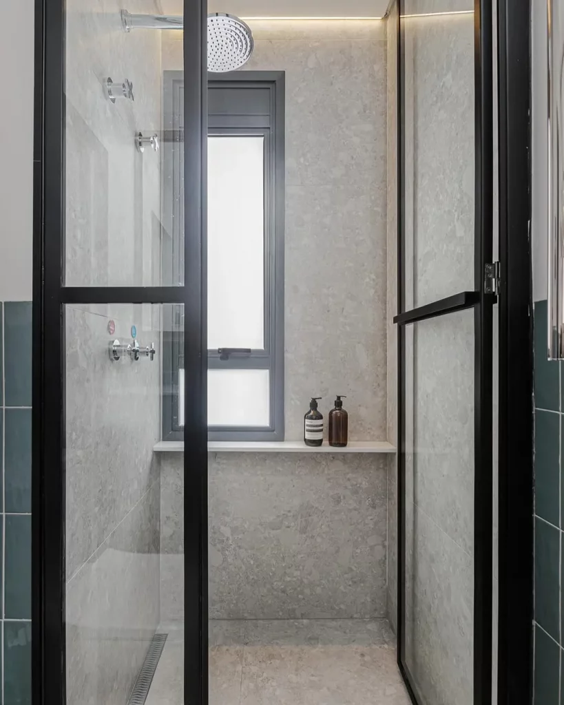 Prateleira branca no box do banheiro e portas pretas de vidro.