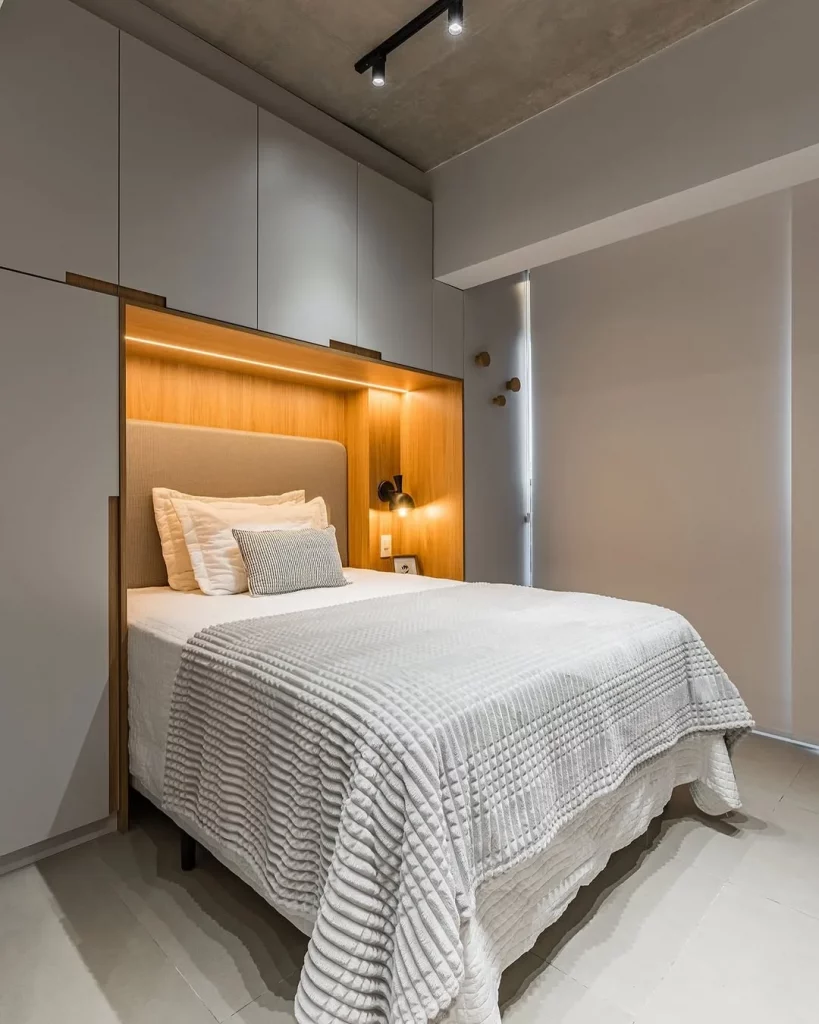 Quarto com cabine na parte da cabeceira, iluminação amarela e armário cinza.