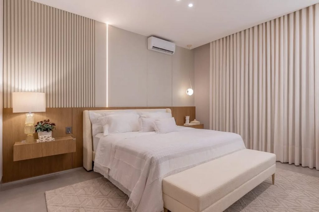 Quarto com luzes brancas, painel na metade da parede e cabeceira branca.