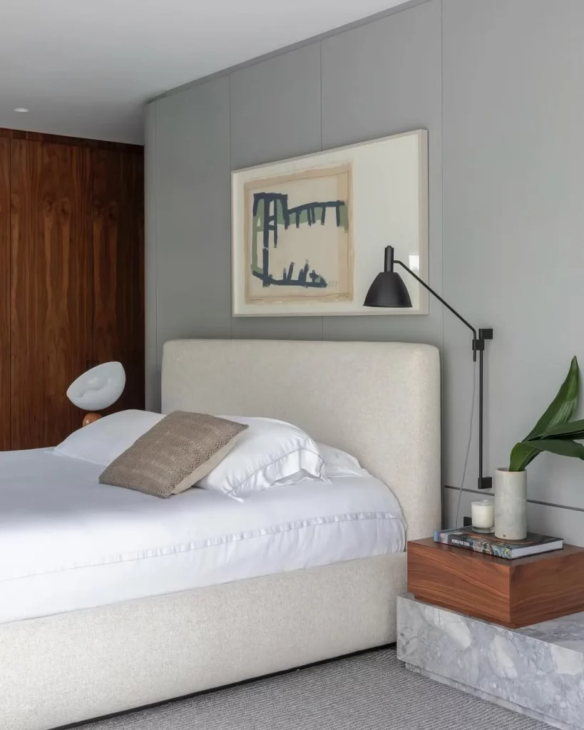 Quarto minimalista com estrutura de cama texturizada, cores neutras e quadro único.
