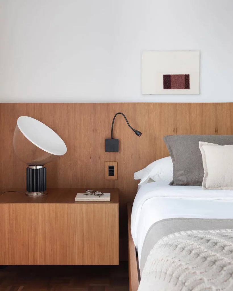 Cabeceira de madeira com luminparia de mesa moderna e quadro simples.