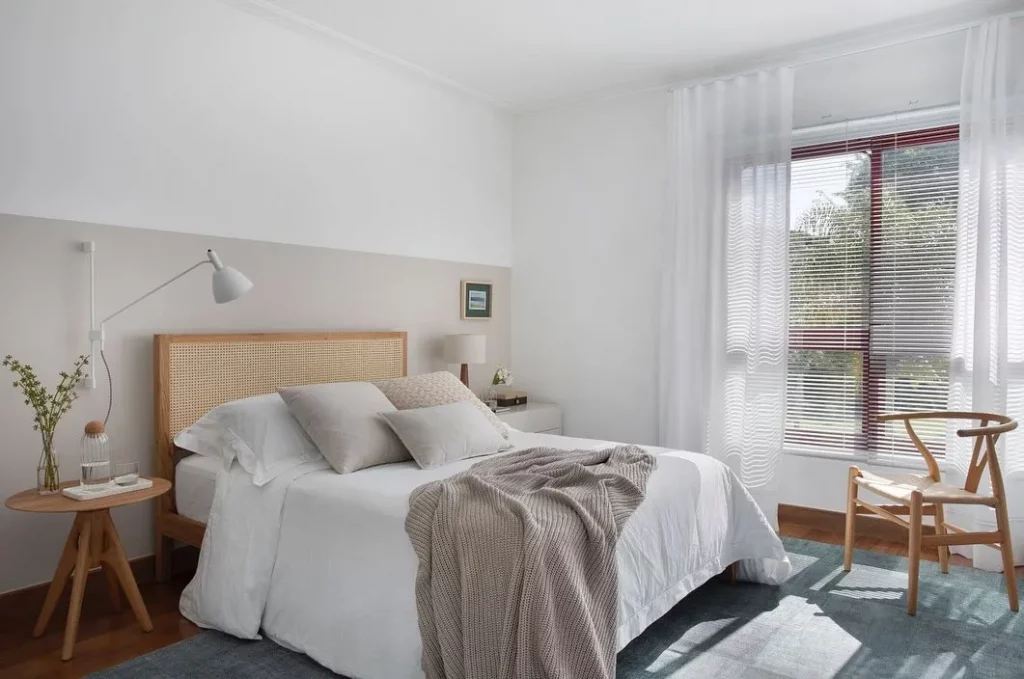Pintura setorizada na parede com cabeceira com palha indiana e roupa de cama cinza.