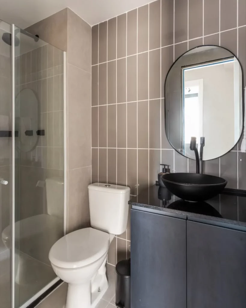 Banheiro pequeno com revestimento marrom e cuba preta.