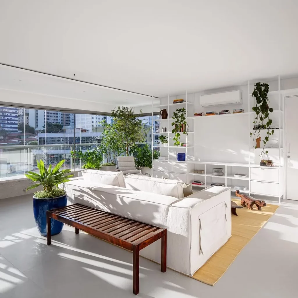 Sala de estar aconchegante com bando de madeira, sofá branco e plantas.