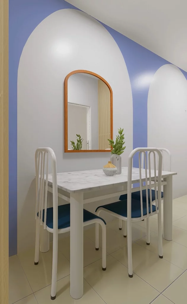 Sala de jantar com mesa com três cadeiras e assento azul, espelho dourado na parede e vaso de plantas pequeno na superfície da mesa.