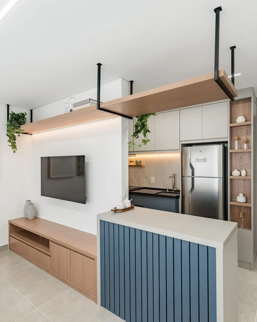 Cozinha e sala conjugada com televisão, plantas e prateleiras, detalhe em azul no balcão.