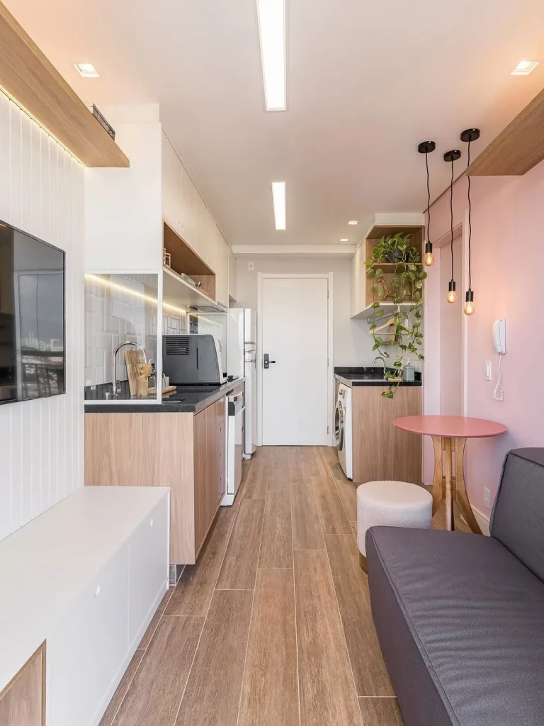 Parede rosa de sala e cozinha integrada, piso de madeira e sofá preto.