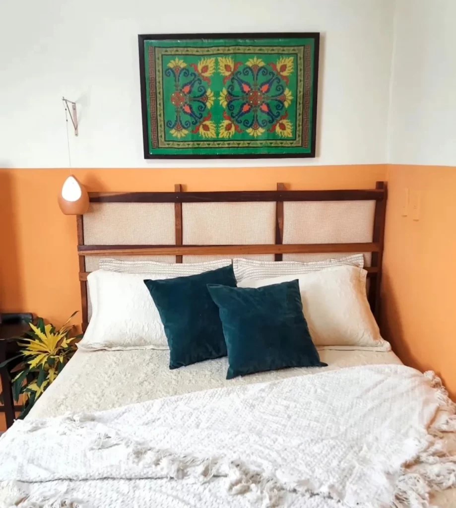 Cabeceira de cama feita com estrado de cama e talagarça, elegante e suave, quadro em cima e parede laranja com branco.