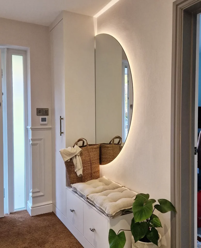 Espelho meia lua iluminado no hall de entrada com banco-baú funcional.