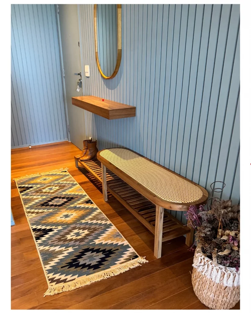 Hall de entrada com painel azul, banco de palha indiana e prateleira suspensa.