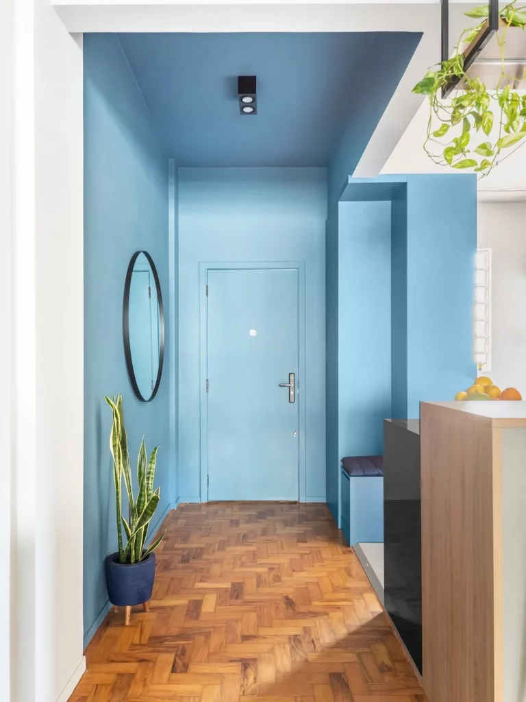 Hall de entrada com paredes azuis e espelho redondo na parede.