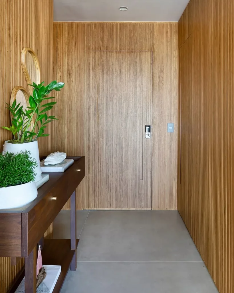 Hall de entrada com vasos de plantas brancos se destacando nas paredes de madeira.