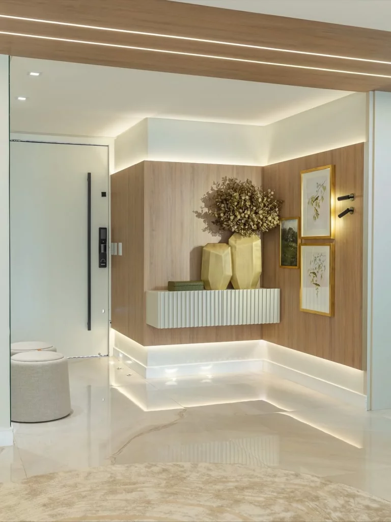 Parede de casa iluminada com fitas de led e arandelas perto dos quadros.