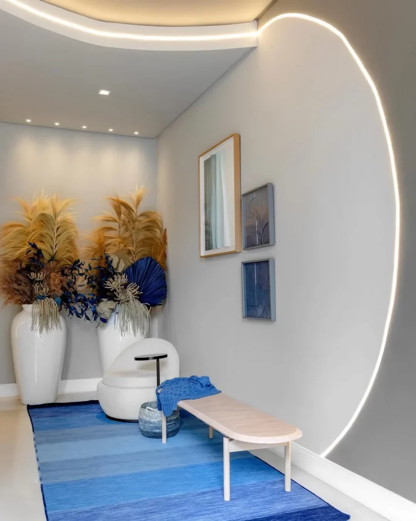 Hall de entrada grande com quadros, banco e vasos.