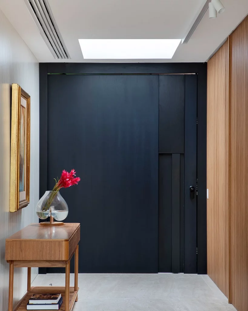 Hall de entrada com porta preta e madeira ao lado na parede.