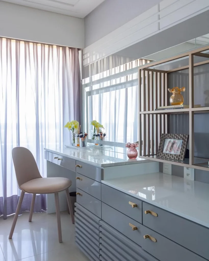 Penteadeira em tom de azul claro com espelho grande e perto da janela.