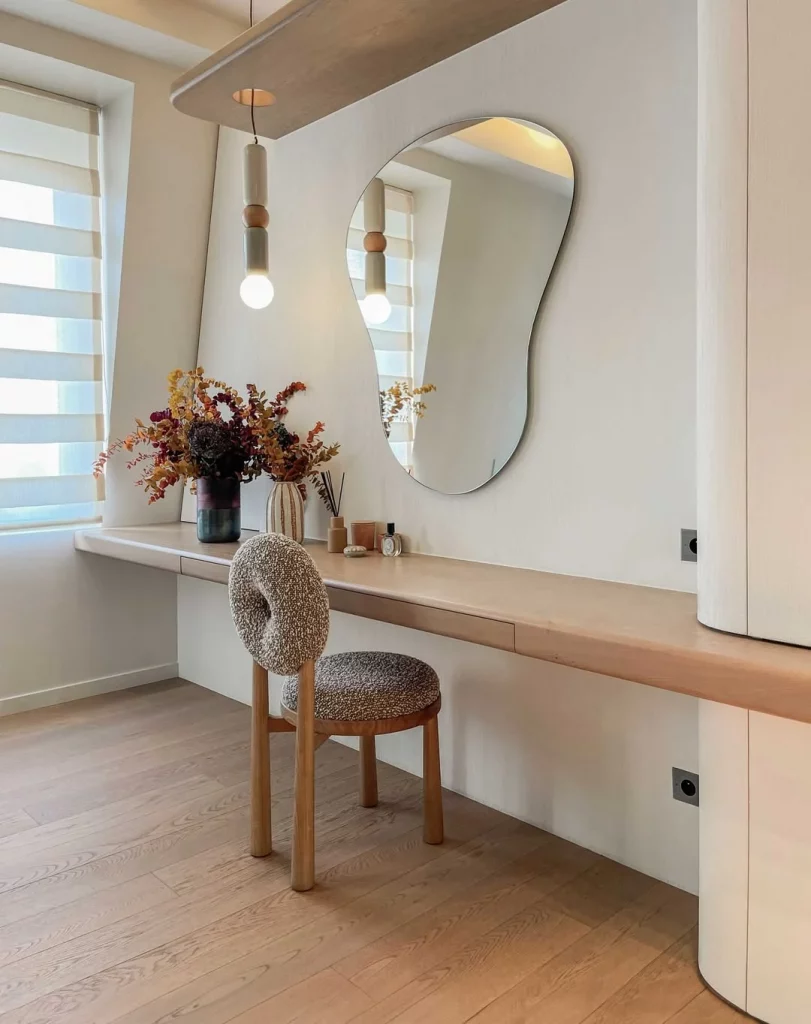 Penteadeira minimalista com espelho orgânico e cadeira cinza.
