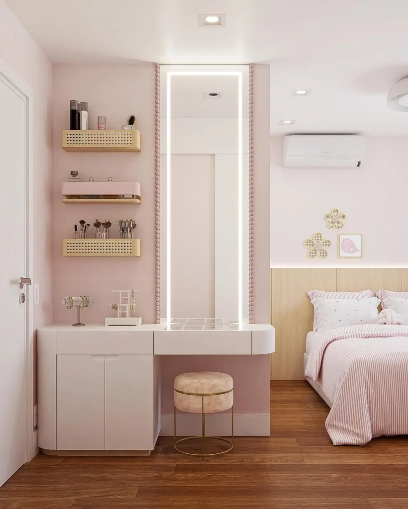 Penteadeira cor de rosa com espelho comprido, prateleiras com palha indiana e banco redondo rosa claro.