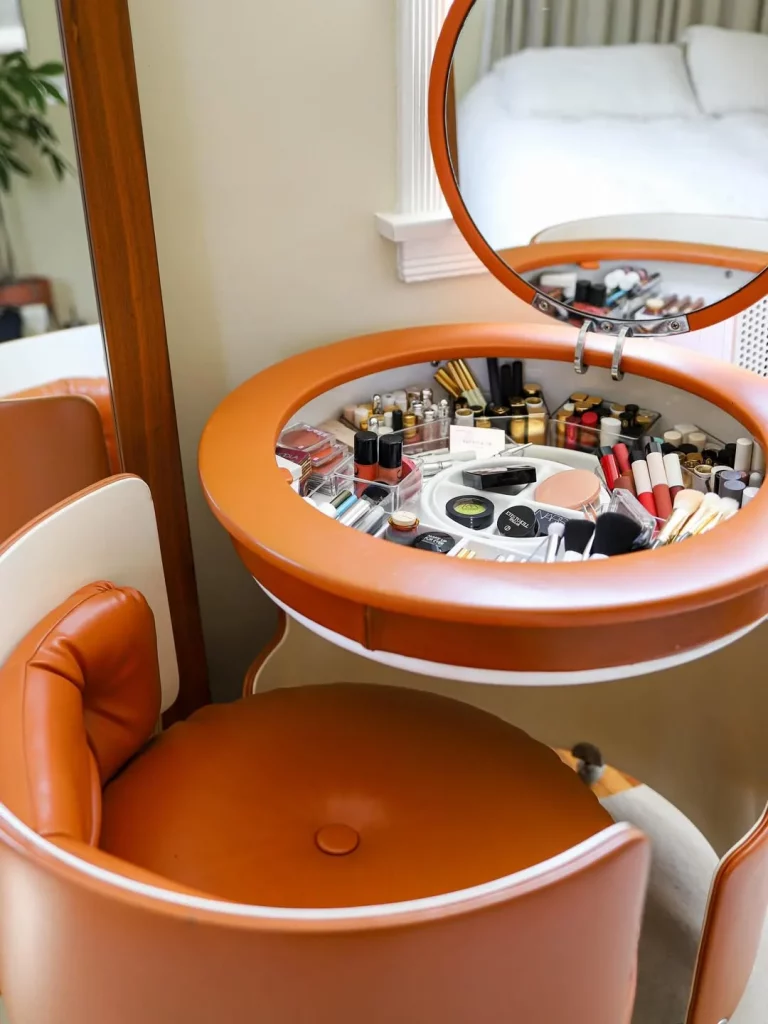 Penteadeira laranja redonda com espelho embutido e interior organizado com várias divisórias.