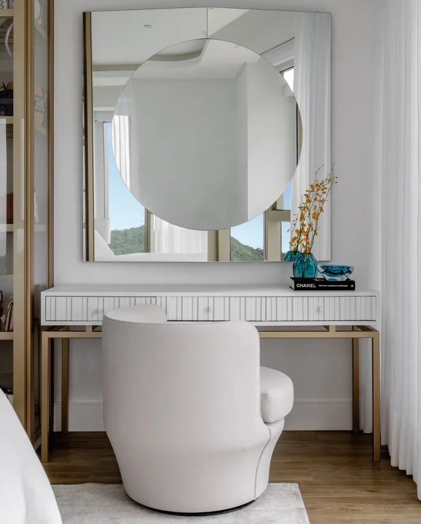 Penteadeira branca elegante com espelho redondo e cadeira branca confortável.