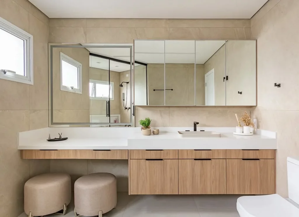 Penteadeira no banheiro com dois puffs e espelho grande.