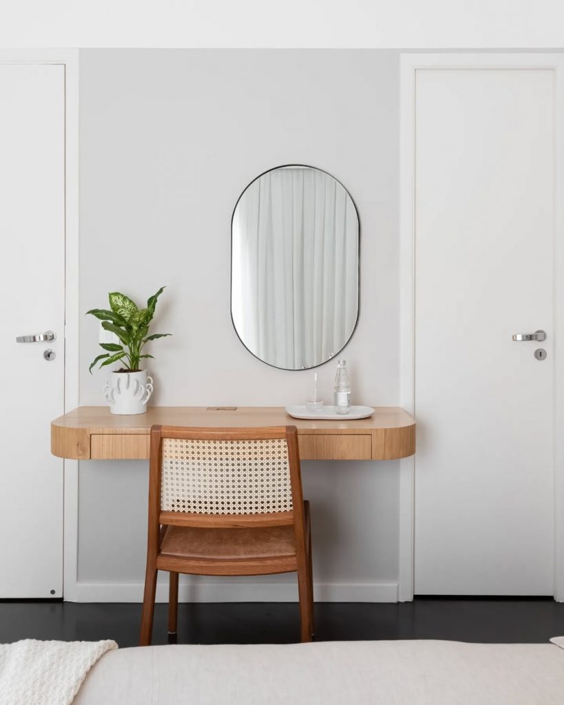 Penteadeira suspensa de madeira com espelho oval e vaso de planta.